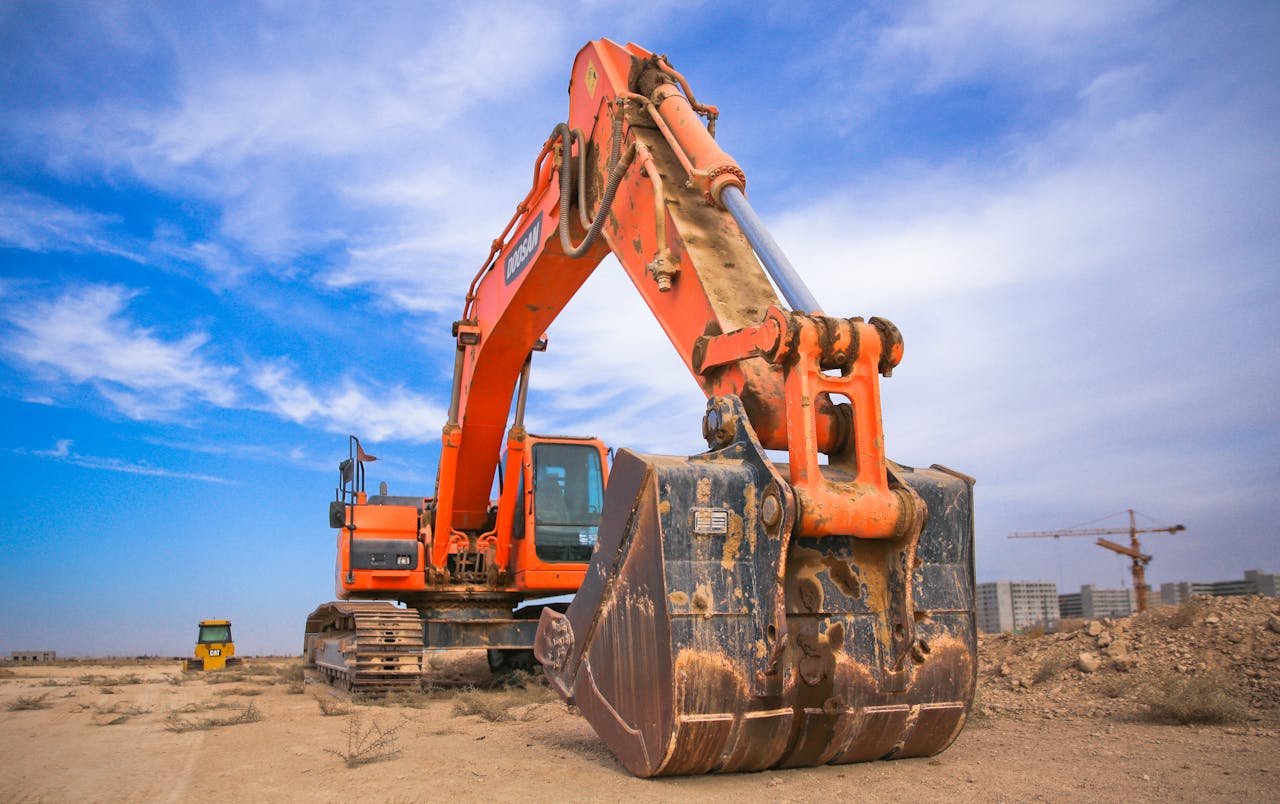 why-choose-us-01 A large orange excavator working on a construction site under a blue sky.
